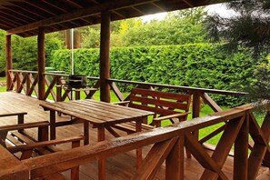 An outdoor wooden deck with picnic tables and benches, surrounded by lush greenery. - Year-round holiday home with fireplace, 3 bedrooms (Kopalino)
