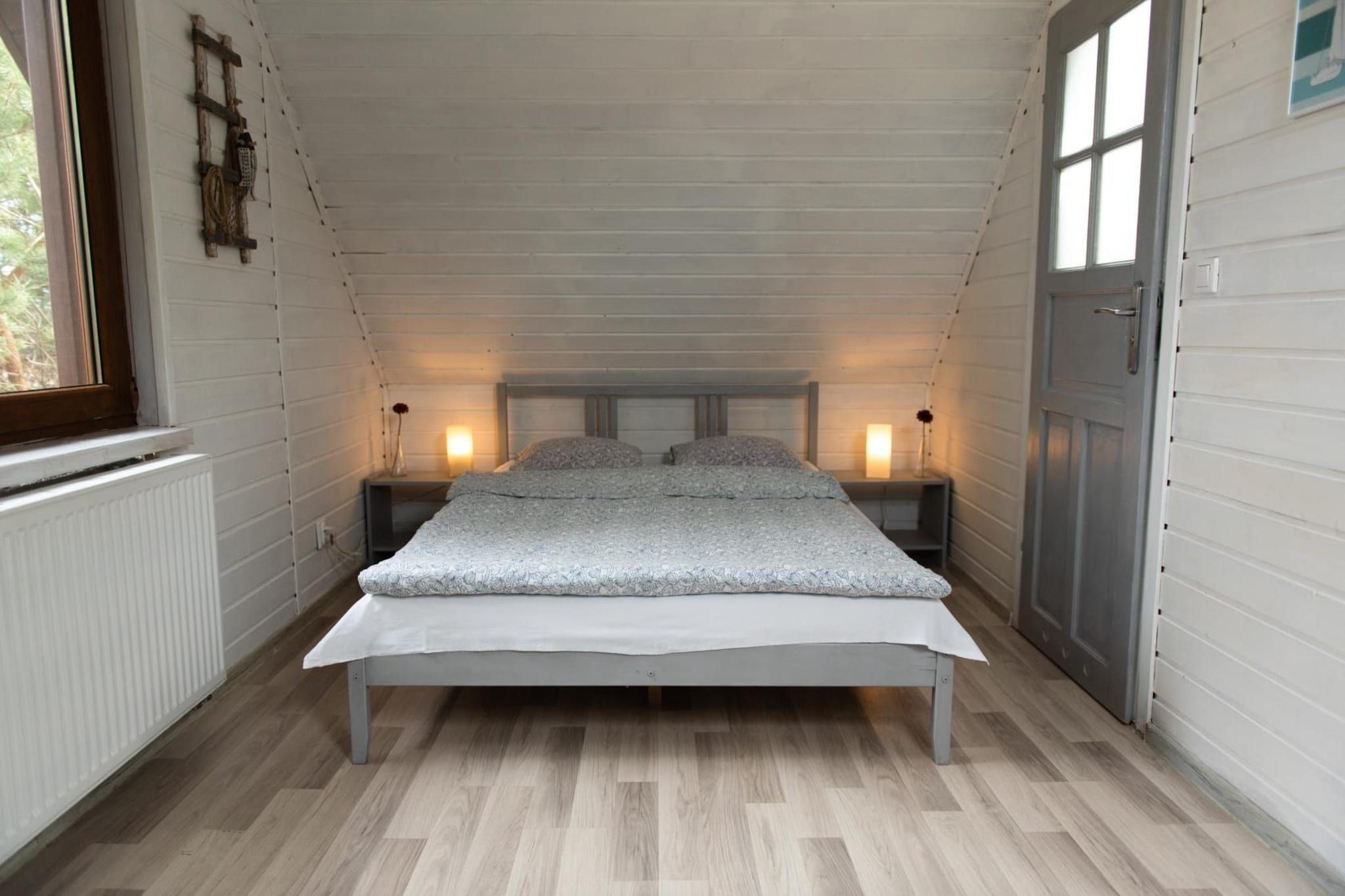 Une petite chambre mansardée comprenant un lit, deux tables de chevet et une fenêtre.