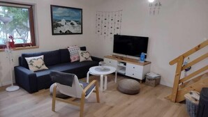 Ein Wohnzimmer mit einer Couch, einem Fernseher, einem Couchtisch und einer Treppe.