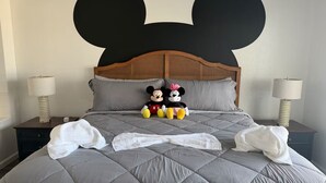 A bed with a large Mickey Mouse head decoration, two Mickey and Minnie Mouse plush toys, and two bedside lamps. - Magical Condohotel at Resort Lake Buena Vista (Orlando)