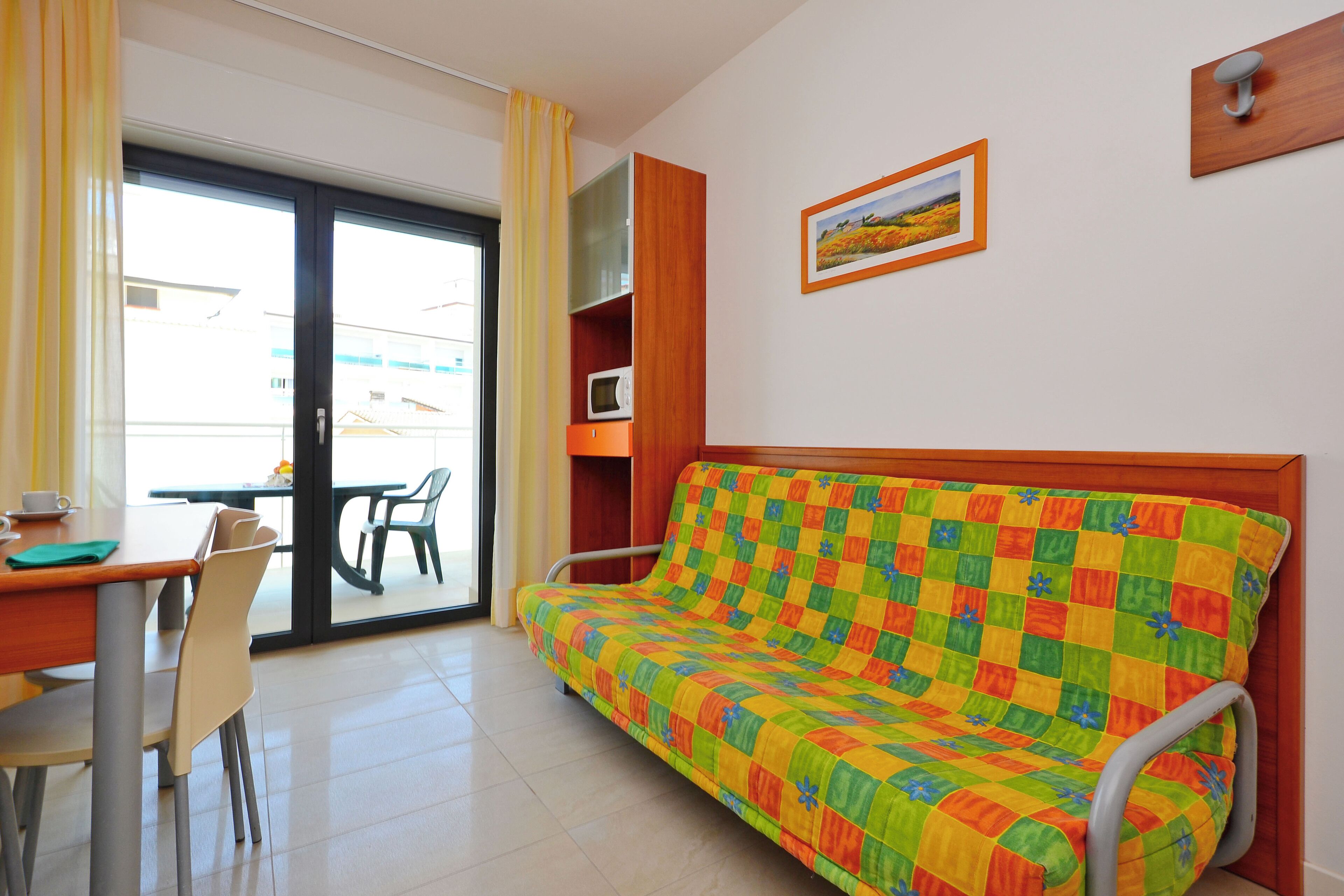 Una habitación con sofá, mesa de comedor, sillas, microondas y vistas a través de un ventanal.
