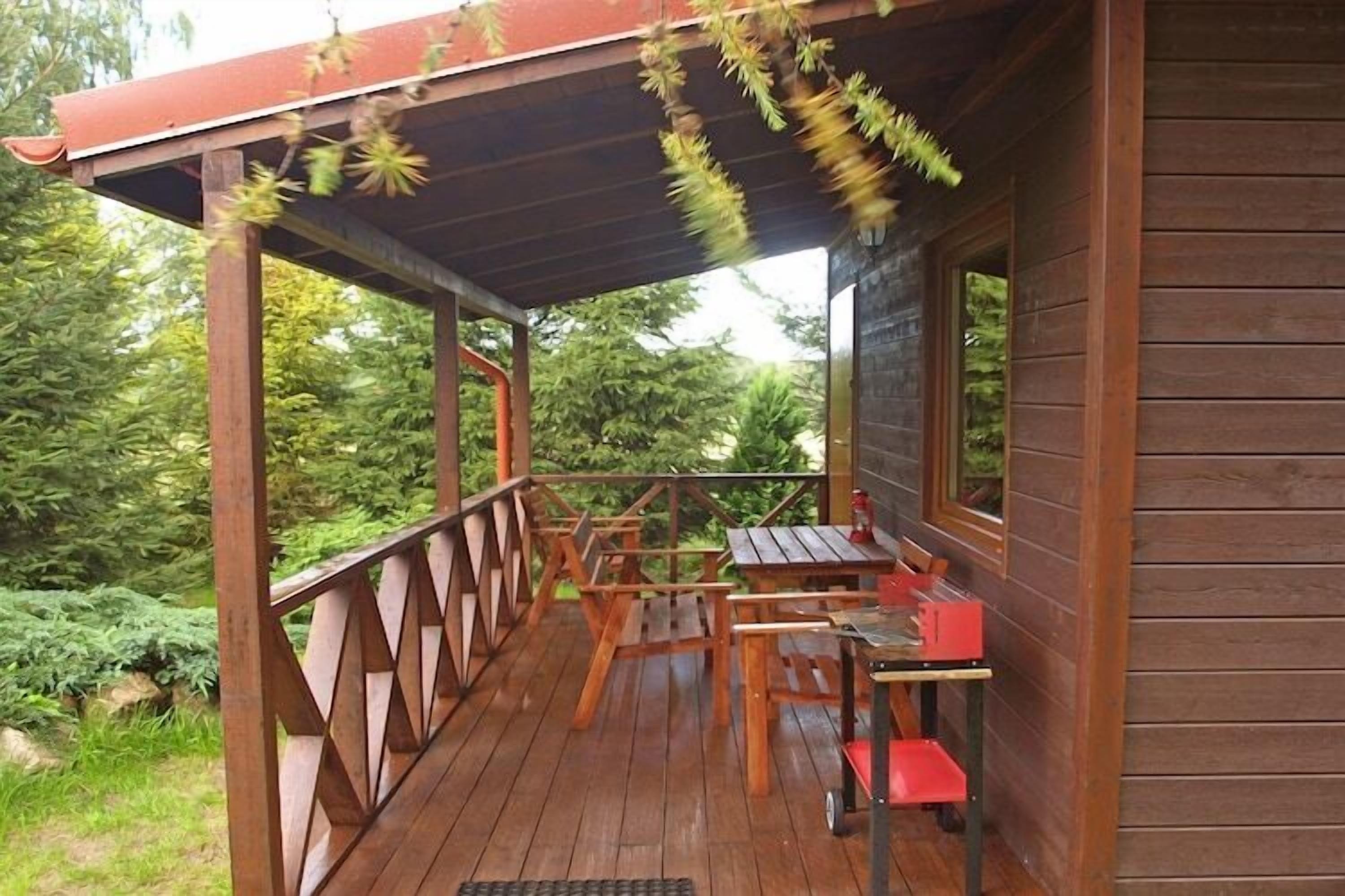 Une terrasse en bois avec une table et des chaises, entourée de verdure.