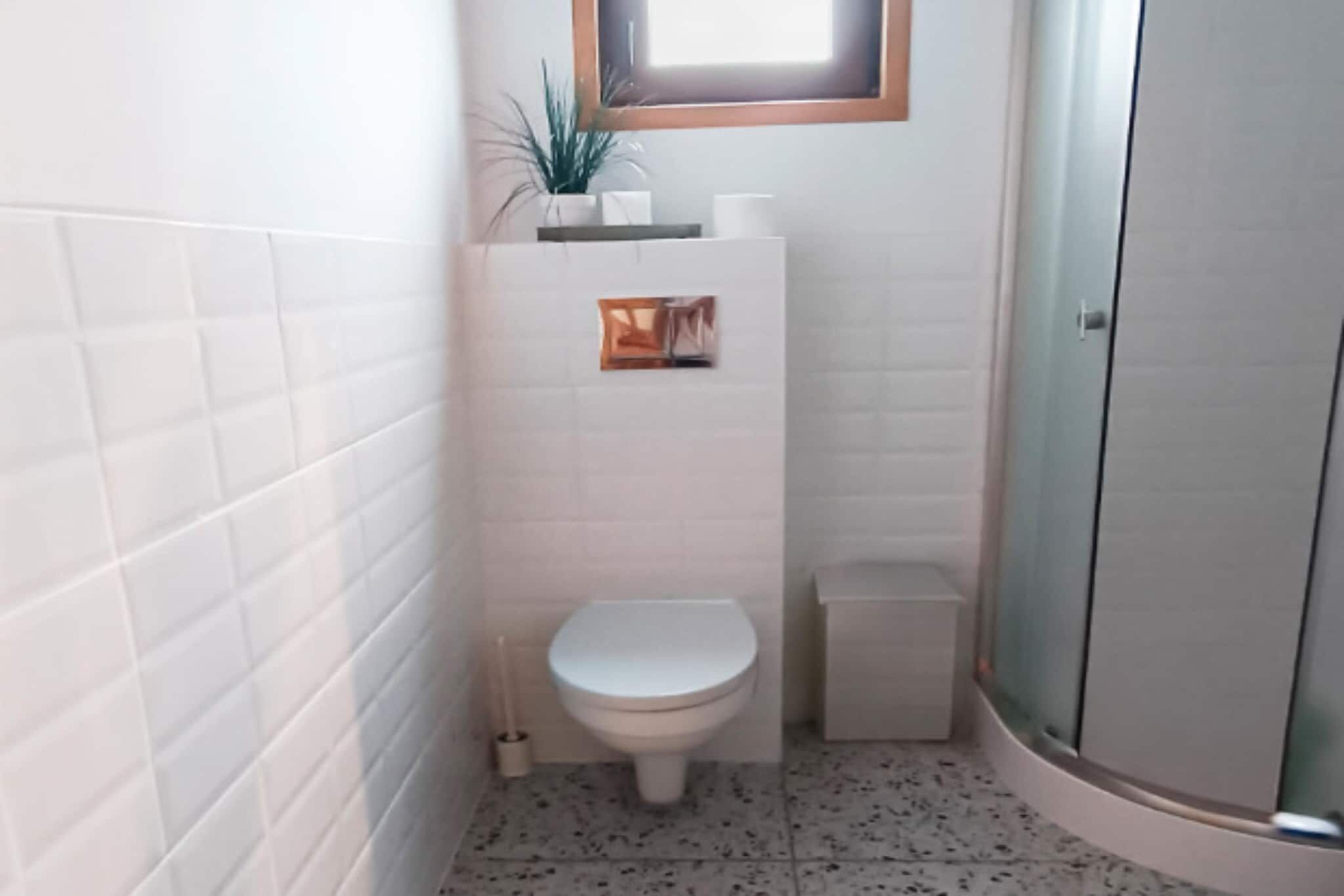 Une petite salle de bain comprenant des toilettes, une petite poubelle et un espace douche.