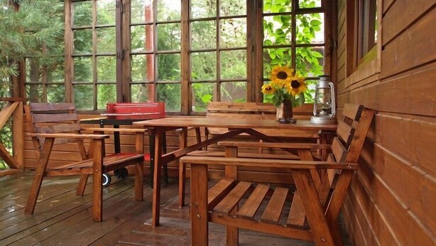 Eine Holzterrasse mit Tisch und Bänken, einer roten Werkzeugkiste und einer Vase mit Sonnenblumen.
