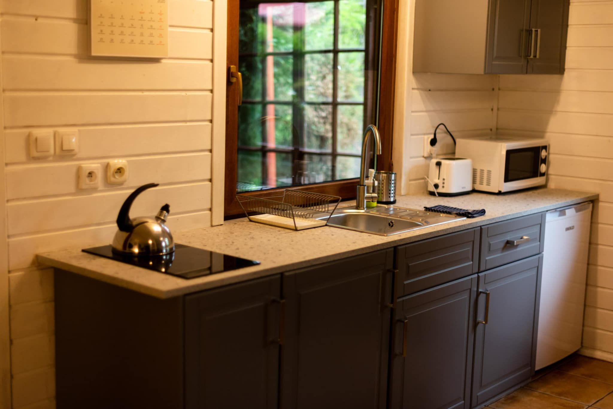 A kitchen with a sink, kettle, toaster, and cabinets.
