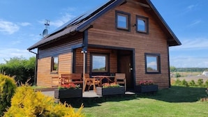 A modern log cabin with a sloped roof, large windows, and a patio with outdoor furniture. - Large, comfortable holiday home with a garden (Smoldzino)