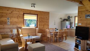 A cozy cabin interior with a sofa, ottoman, dining table, chairs, a TV stand, and a kitchen area. - Large, comfortable holiday home with a garden (Smoldzino)
