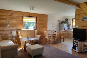 A cozy cabin interior with a sofa, ottoman, dining table, chairs, a TV stand, and a kitchen area. - Large, comfortable holiday home with a garden (Smoldzino)