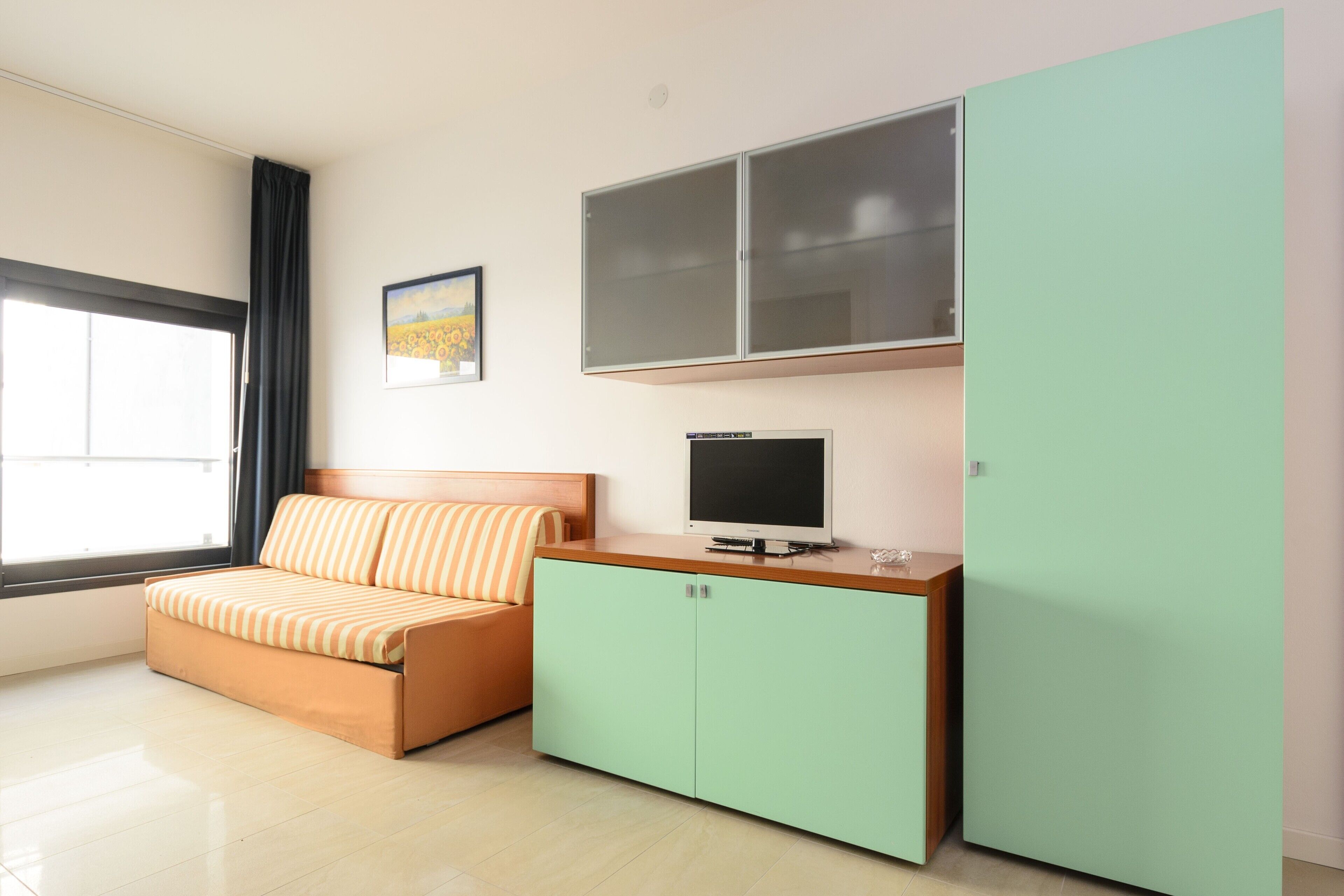 A room with a bed, a television, a cabinet, and a window.