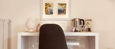 Una habitación moderna con un escritorio blanco, una silla negra, un espejo y dos cuadros en la pared.