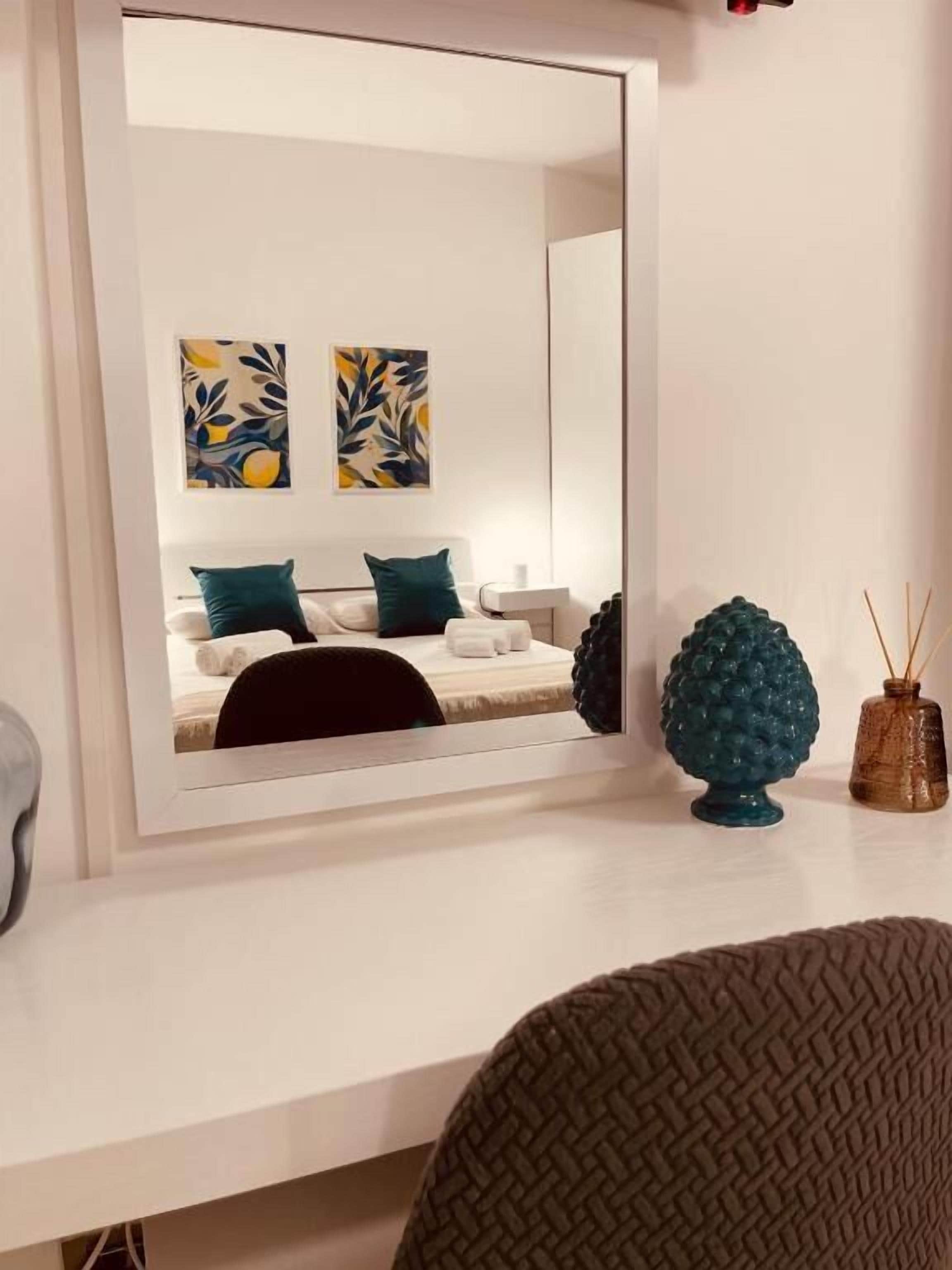 A modern room with a large mirror, a sofa, two abstract paintings, and decorative items on the mantel.