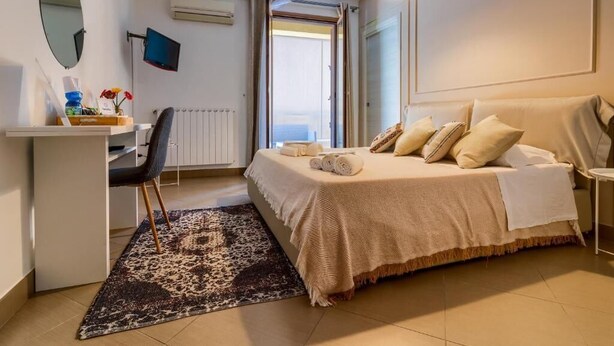 A bedroom with a bed, a desk, a chair, a TV, a window, and a radiator. - KANISA MARI E MONTI (Cinisi)