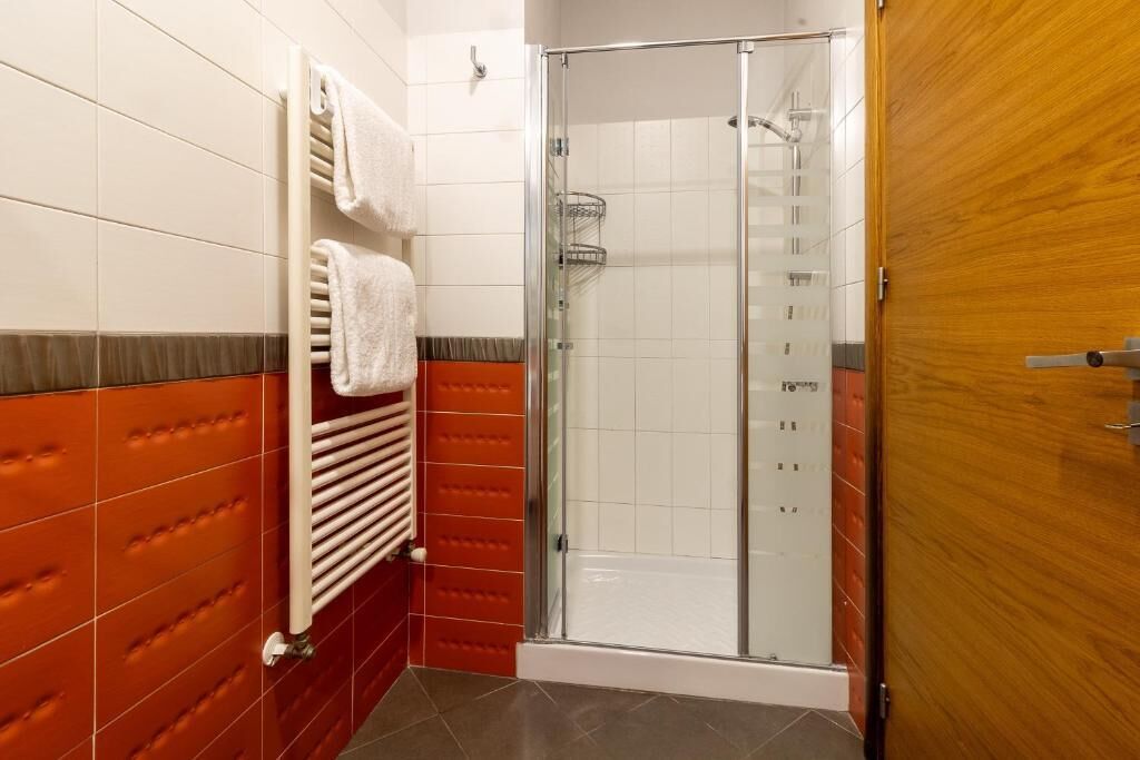 A shower with a glass door, a towel rack with towels, and a wooden door.