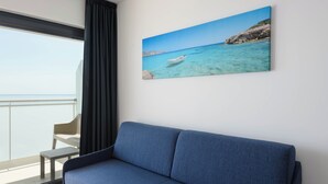Una stanza moderna con un divano blu, un quadro raffigurante una costa marina e vista sul mare attraverso una finestra.