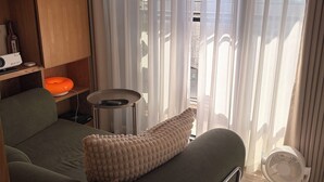 A room with a green sofa, a small table, a white fan, and a view through sheer curtains. - Luxury Sunset River View / Quiet & Convenient / Ximen / Monthly Rentals (Taipei City)