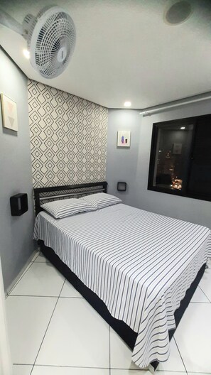 A bedroom with a bed, a wall-mounted fan, a patterned wall, a window with a view, and a framed picture. - Cozy studio in downtown São Paulo. (São Paulo)