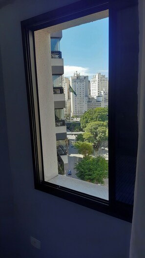 A window with a view of a cityscape, including buildings and a tree-lined street. - Cozy studio in downtown São Paulo. (São Paulo)