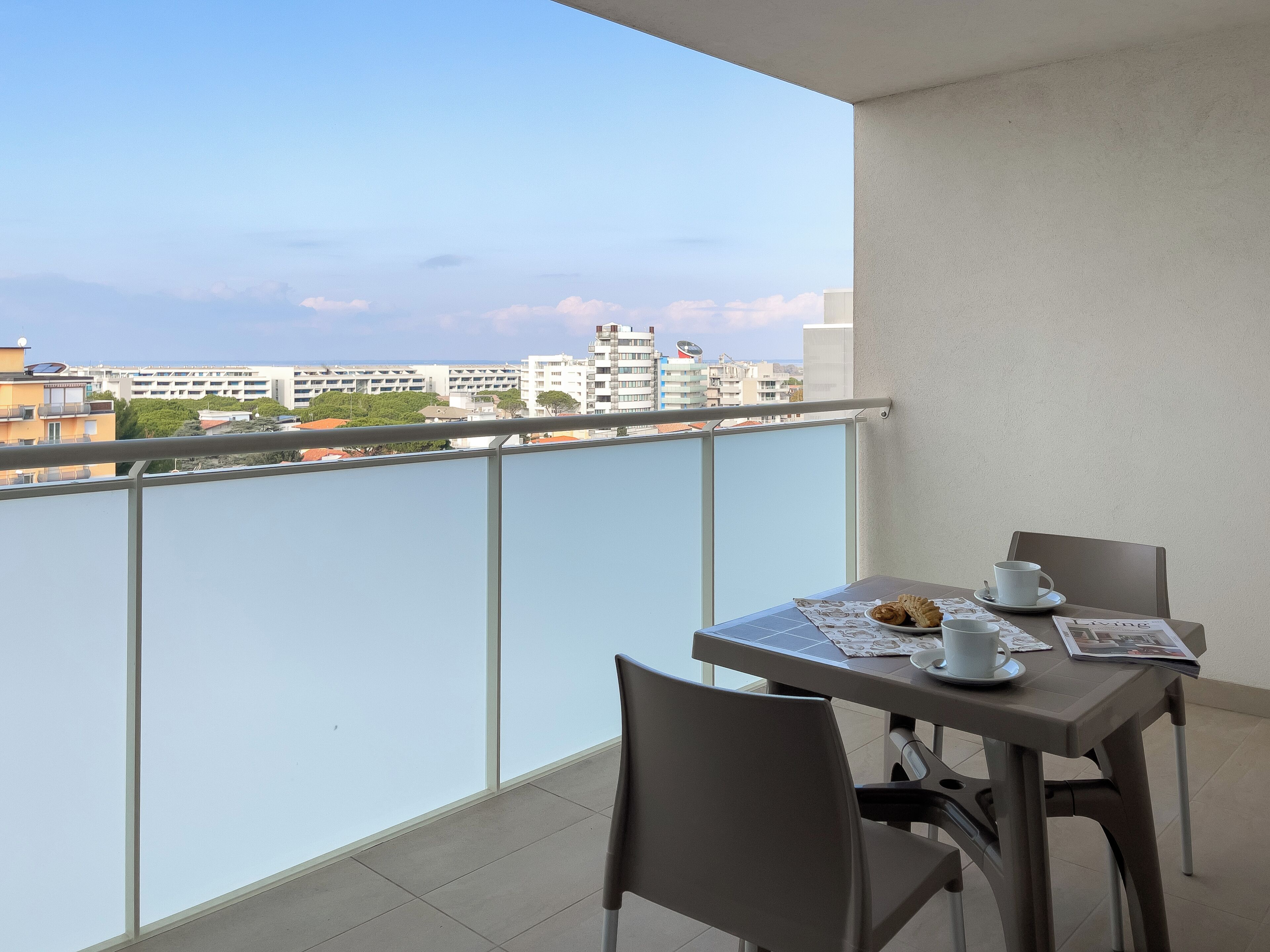 A balcony with a table set for two, a chair, and a view of the cityscape.