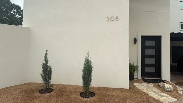 A modern building with a white facade, a black door, and the number 308. There are two potted plants in front.