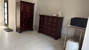 A room with a large dark wooden cabinet, a white trash bin, and a metal cart.