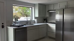 A modern kitchen with white cabinets, stainless steel appliances, and a window providing natural light.