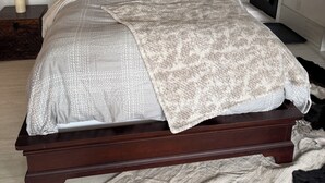 A bed with a patterned bedspread, a bedside table with a candle, and a mirror on the wall.