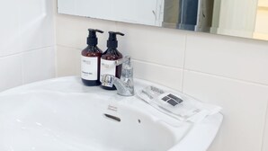 Un lavabo de salle de bain avec deux bouteilles de gel douche, un robinet argenté et un bonnet de douche posé sur le comptoir.