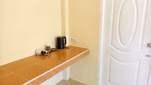 Une salle de bain avec un comptoir carrelé, une machine à café, une poubelle et une porte blanche.
