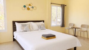 Une chambre d’hôtel comprenant un lit, une petite table, deux chaises, une fenêtre avec des rideaux et un élément de décoration murale.