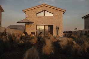 Une maison en pierre avec un toit en tuiles, une porte vitrée et une terrasse aménagée avec du mobilier d’extérieur.