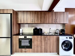 A compact kitchen with wooden cabinets, a built-in dishwasher, a washing machine, and a refrigerator. - STAY Finikoudes Nest 1 (Larnaca)