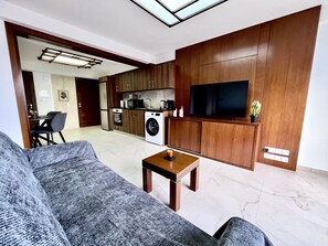 A modern living room with a sofa, a coffee table, and a TV mounted on a wooden wall. - STAY Finikoudes Nest 1 (Larnaca)