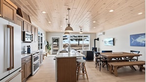 A modern kitchen with wooden cabinets, a central island, and a dining area with a wooden table and chairs.