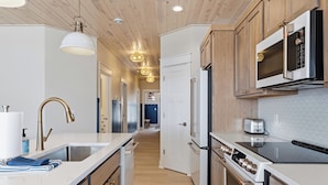 A modern kitchen with wooden cabinets, stainless steel appliances, and pendant lighting.