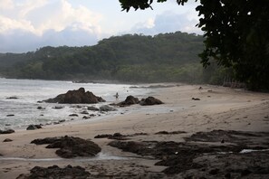 A beach with rocky outcrops and a forested hillside in the background. - Jungle Canopy Bungalow at Taru Rentals (Montezuma)