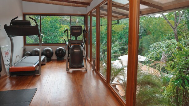 A gym with exercise equipment, a treadmill, and large windows overlooking a garden. - Jungle Canopy Bungalow at Taru Rentals (Montezuma)