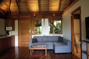 A modern living room with a sectional sofa, wooden flooring, a coffee table, and a television. - Jungle Canopy Bungalow at Taru Rentals (Montezuma)