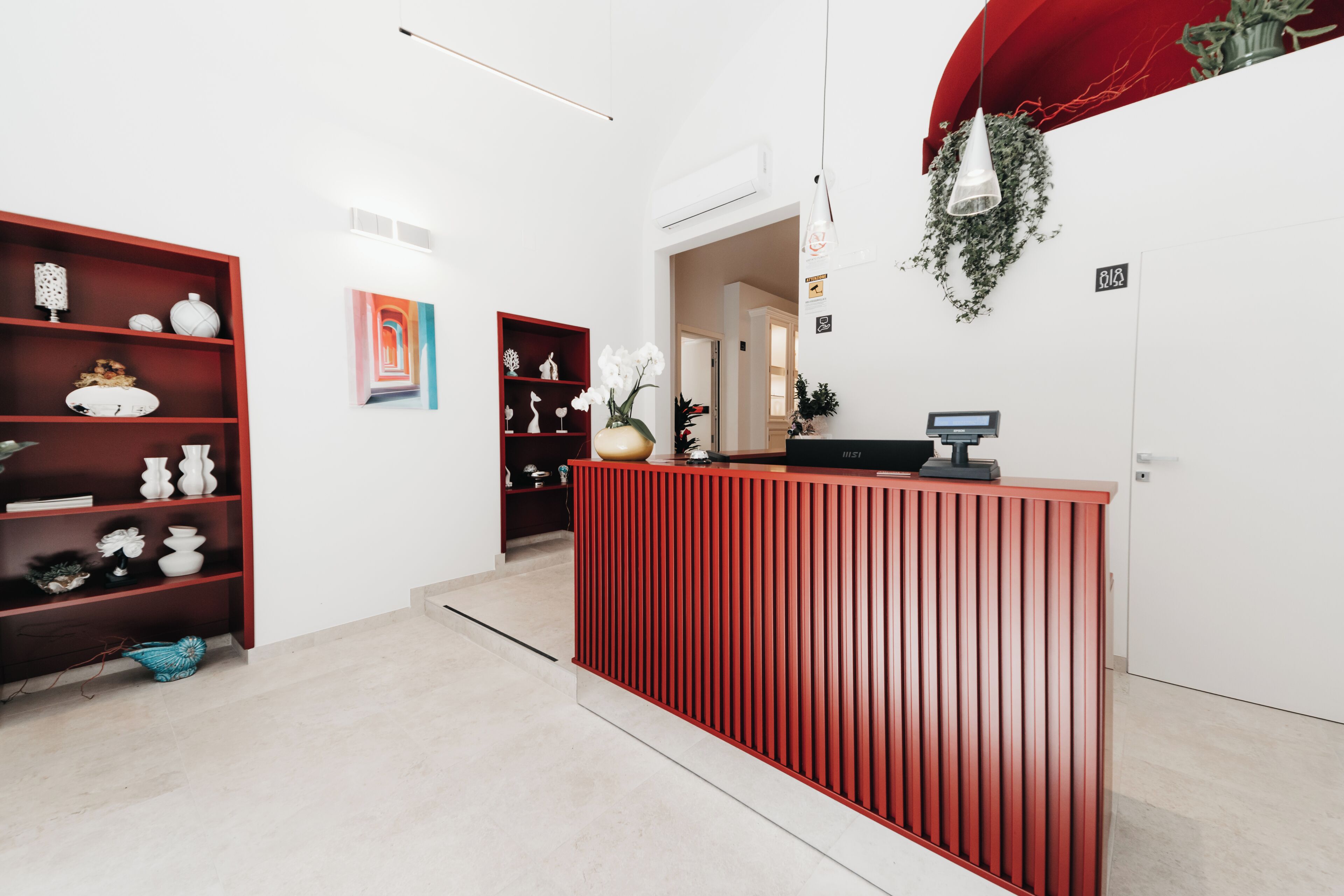 Una recepción con detalles en rojo, una pared blanca con una obra enmarcada y un estante rojo decorado con objetos.