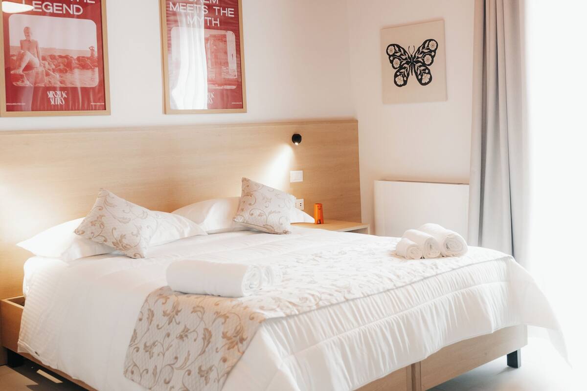 Una habitación de hotel moderna con una cama grande, una mesita de noche, una lámpara y dos carteles en la pared.