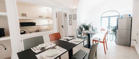 A modern kitchen with white cabinetry, a dining area with a black table, and a view through an archway to a balcony.