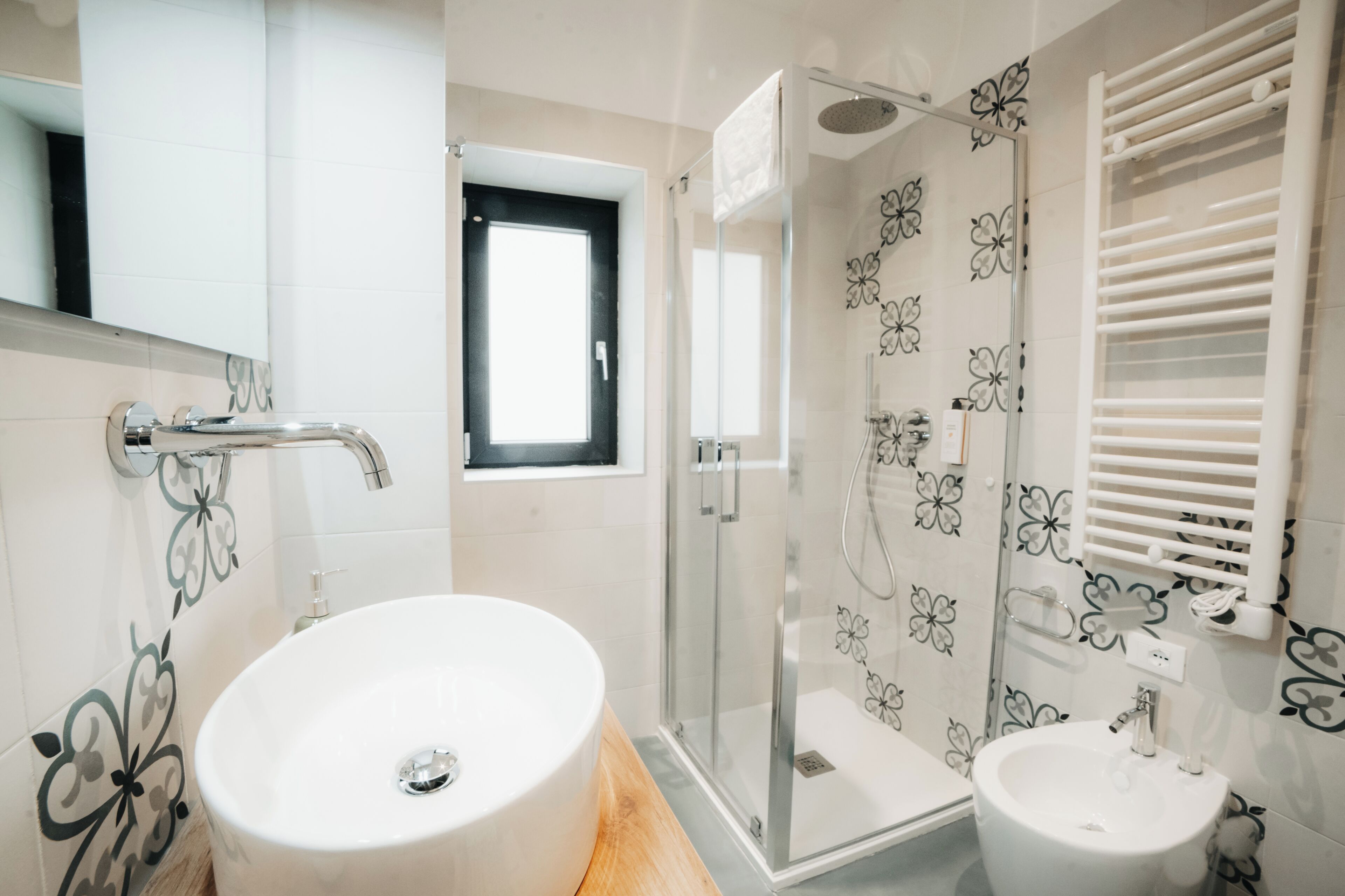 A bathroom with a round sink, a glass-enclosed shower, and a small window.