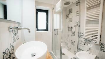 A bathroom with a round sink, a glass-enclosed shower, and a small window.