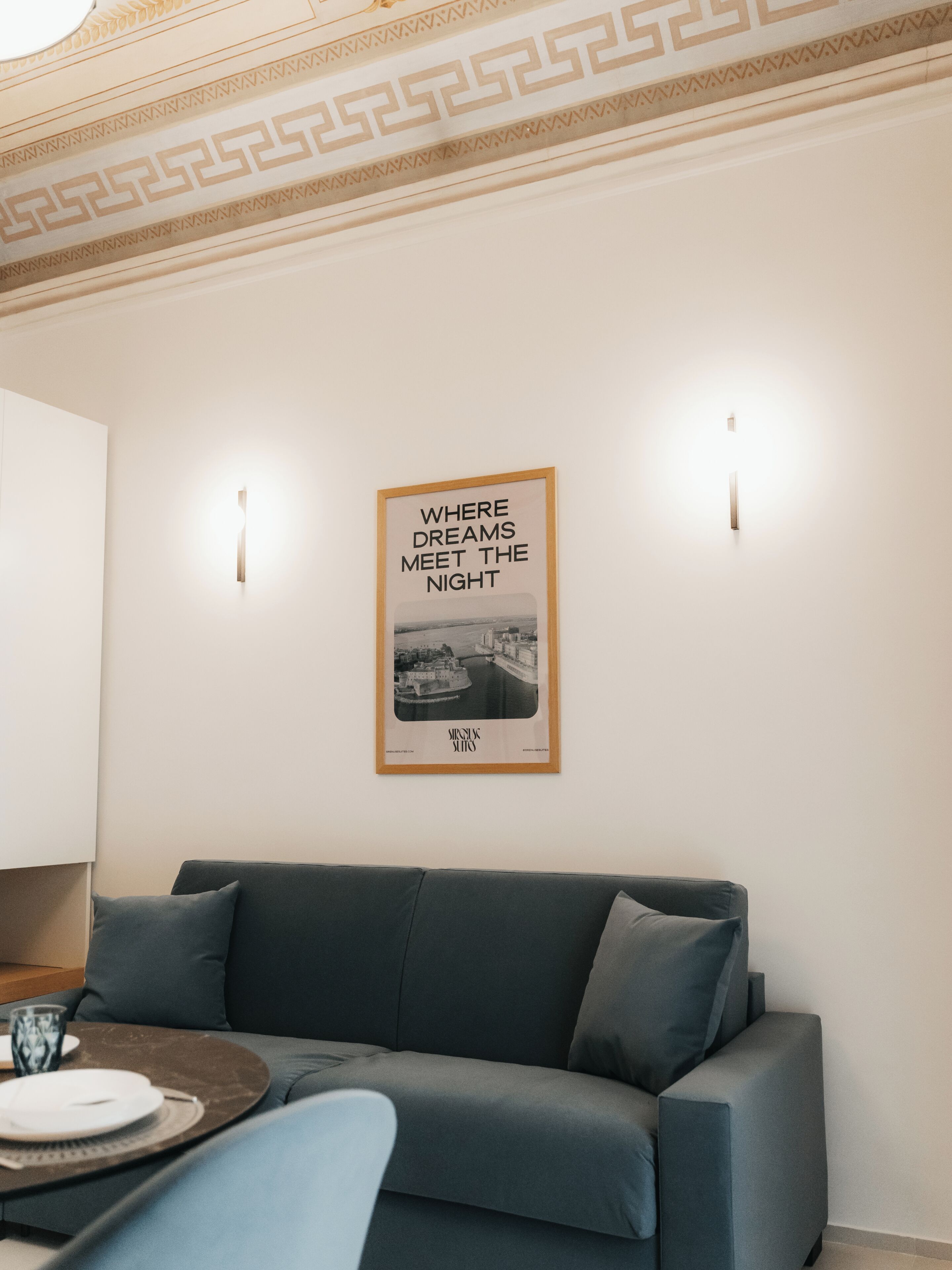 Ein Zimmer mit einem grauen Sofa, einem gerahmten Bild an der Wand und einer Lampe auf der linken Seite.