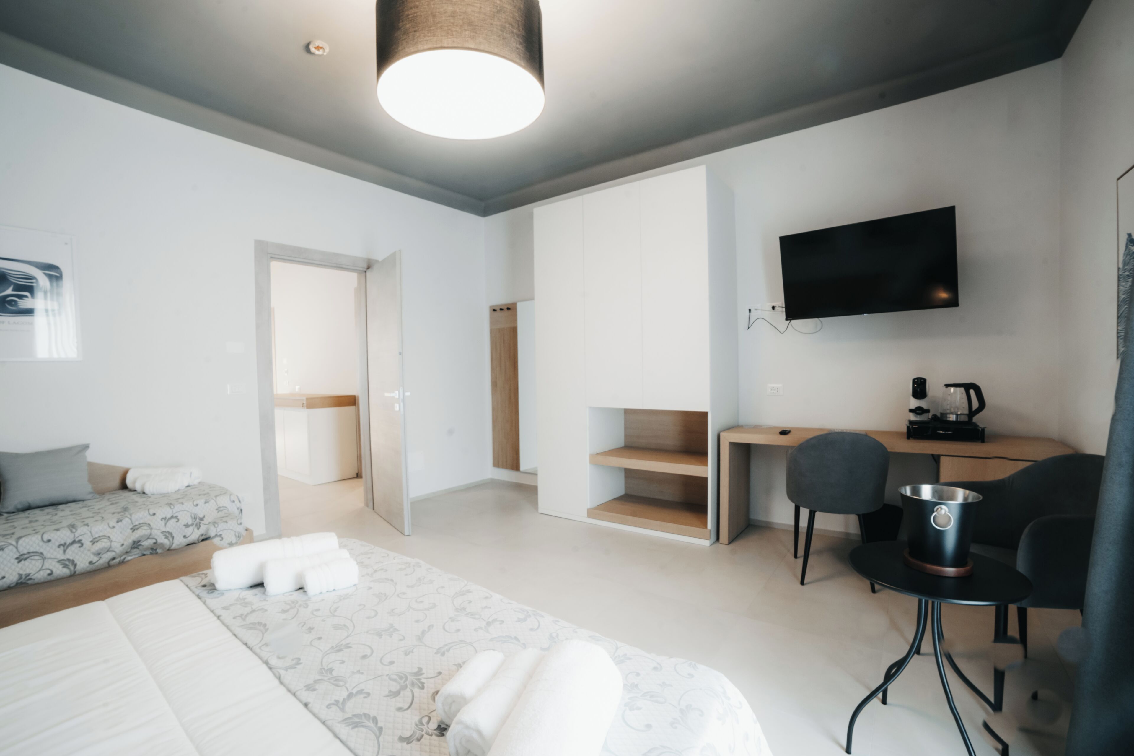 A modern hotel room with a bed, a desk, a chair, a TV, and a kitchenette.