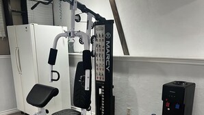 Ein Heimfitnessraum mit einem multifunktionalen Trainingsgerät, einem Wasserspender und einer großen Wasserflasche.