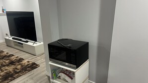 Ein modernes Wohnzimmer mit Fernseher, einer Mikrowelle auf einem weißen Schrank, einem Mülleimer und einem hochflorigen Teppich.