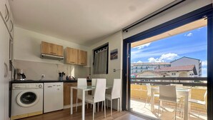 A compact kitchen with a washing machine, wooden cabinets, and a dining area with white chairs. - Seafoam - T1 BIS near the ocean (Mimizan)