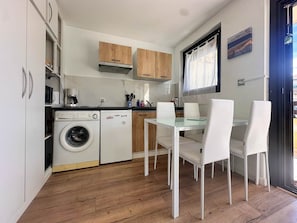 Eine kompakte Küche mit Waschmaschine, Holzschränken, einem Esstisch mit Glasplatte und weißen Stühlen.