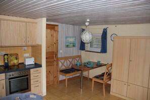 A compact kitchen with wooden cabinets, a built-in oven, and a dining area with a table and chairs. - Apartment 2 Garden Geltinger Bucht - relaxation near the beach & nature (Gelting)