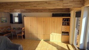 Ett rum med en garderob i trä, ett bord med stolar, en bänk och ett fönster med gardiner.